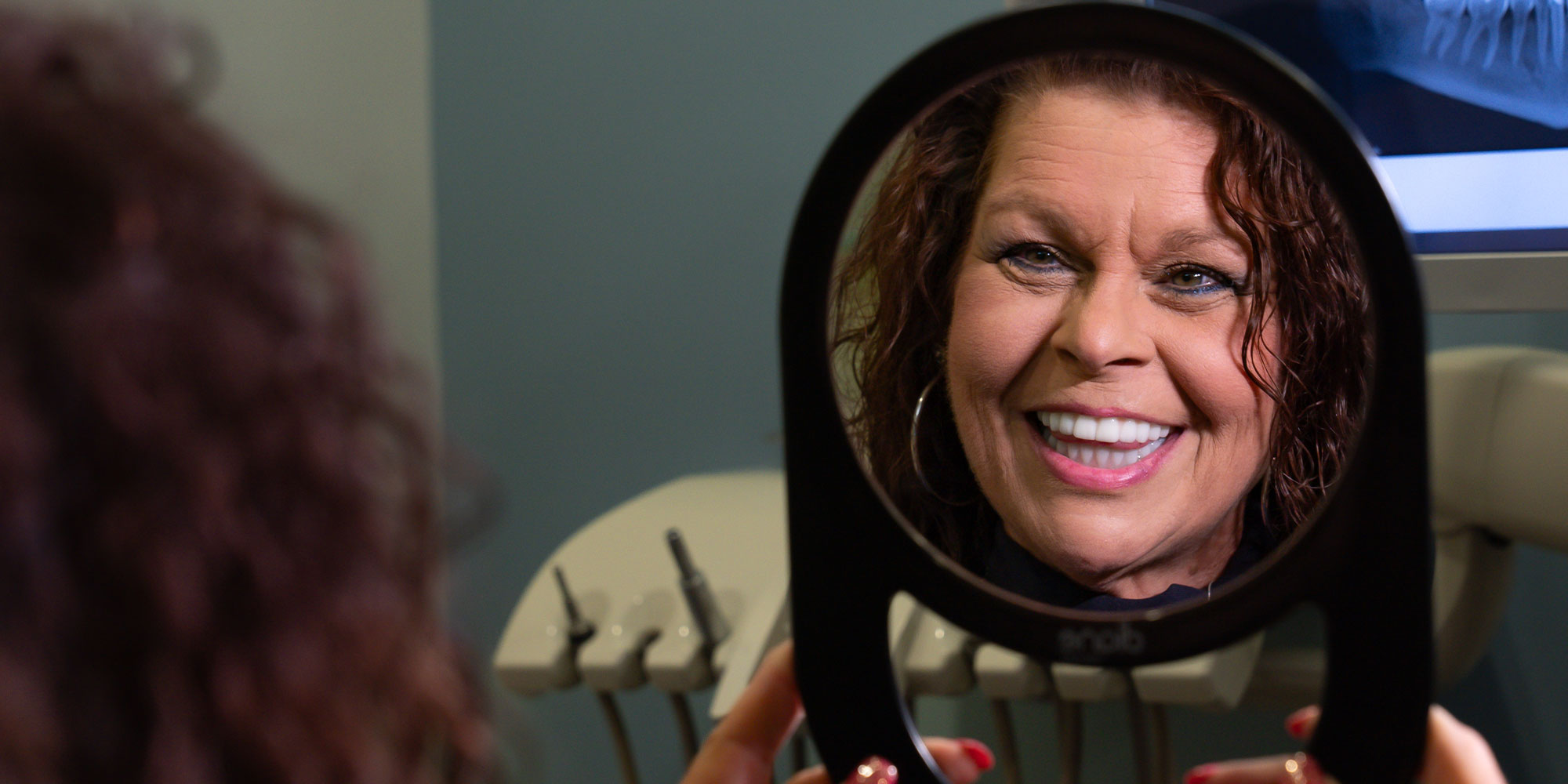 patient smiling brightly in a handheld mirror