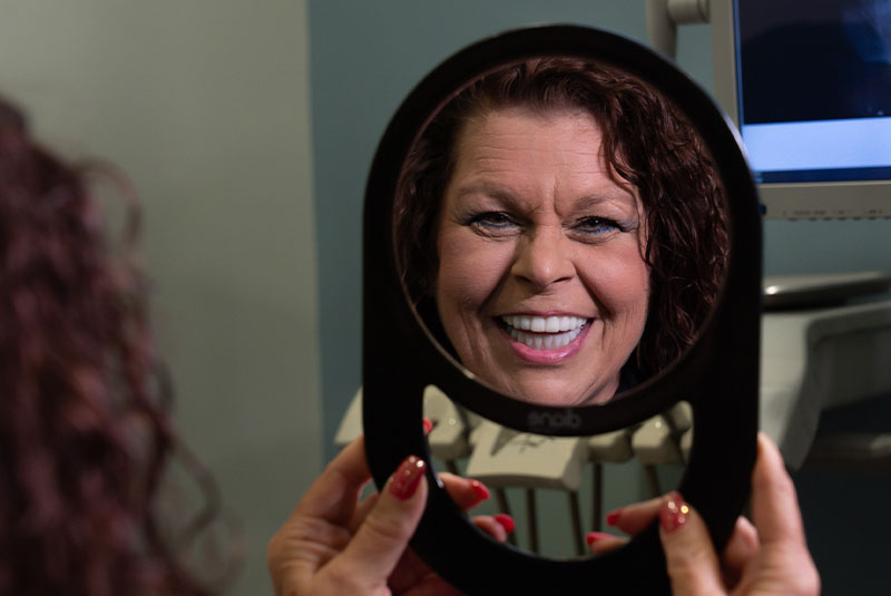 patient smiling brightly in a handheld mirror